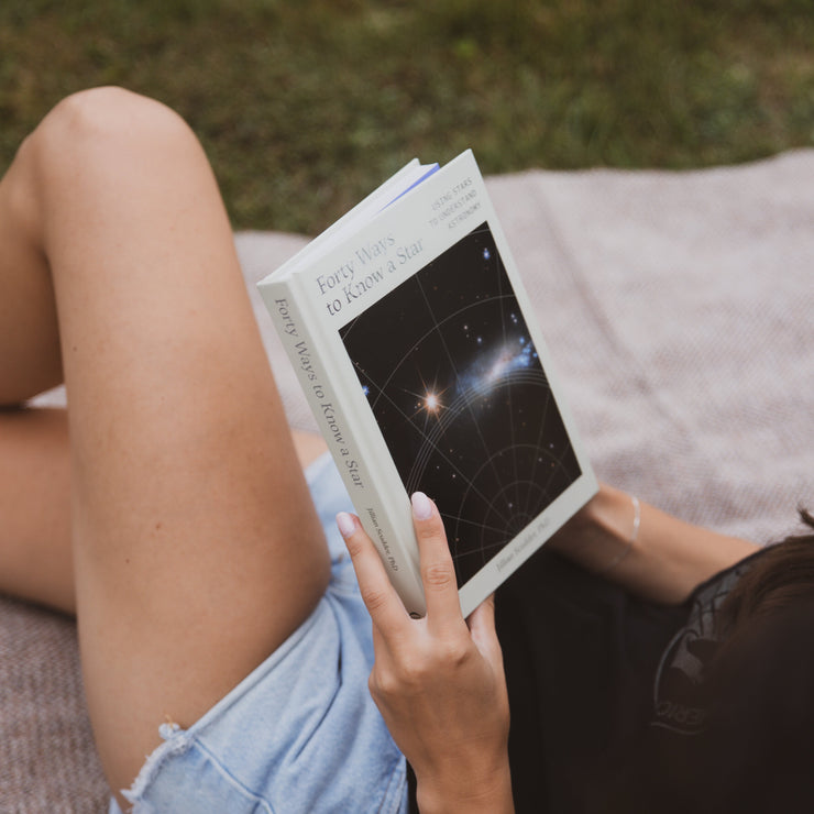 A person on a blanket outside reading forty ways to know a star