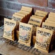 Bags of Gem & Honey bath salt on a wooden surface with a brick wall background