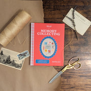 Book titled 'The Art of Memory Collecting' on a wooden surface with photos, twine, and scissors.