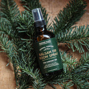 Balsam fir room spray bottle with green label on a wooden surface with pine branches