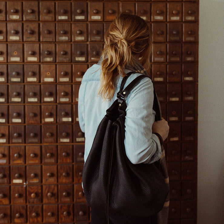 Model wearing a black drawstring backpack in front of a set of drawers