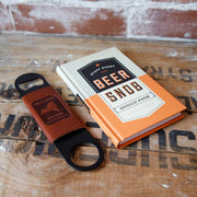 Book titled 'Beer Snob' and leather bottle opener on a wooden surface with visible branding.