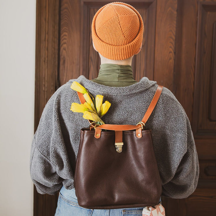 brown leather backpack that converts with flowers on a model