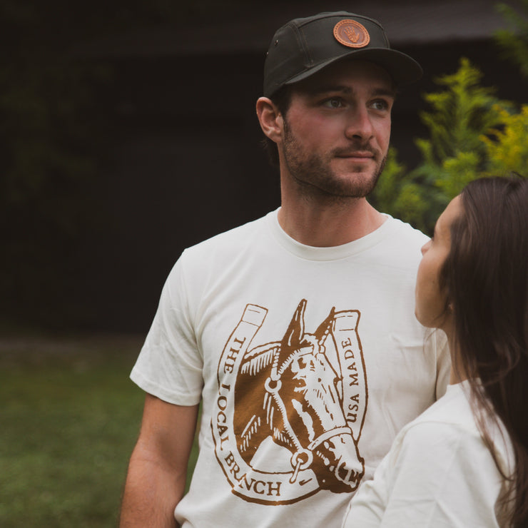 Man wearing a t-shirt with a horse graphic and text, standing outdoors with a blurred background