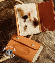 Two views of the fly fisherman's wallet open and closed next to a fishing next with fishing hooks and flies 