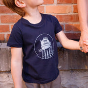 Child wearing a navy blue t-shirt with a graphic design of a water tower that reads home of the lakers, holding hands with an adult against a brick wall.