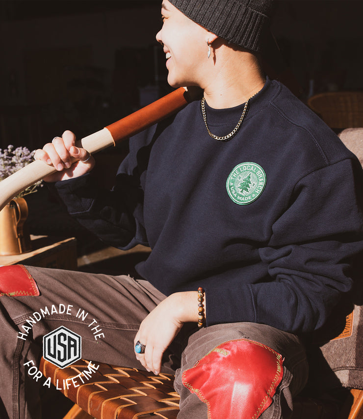 Pine tree on a patch that reads the local branch ny USA made. Green patch with white details. On a black heavy weight 100% cotton crewneck sweatshirt