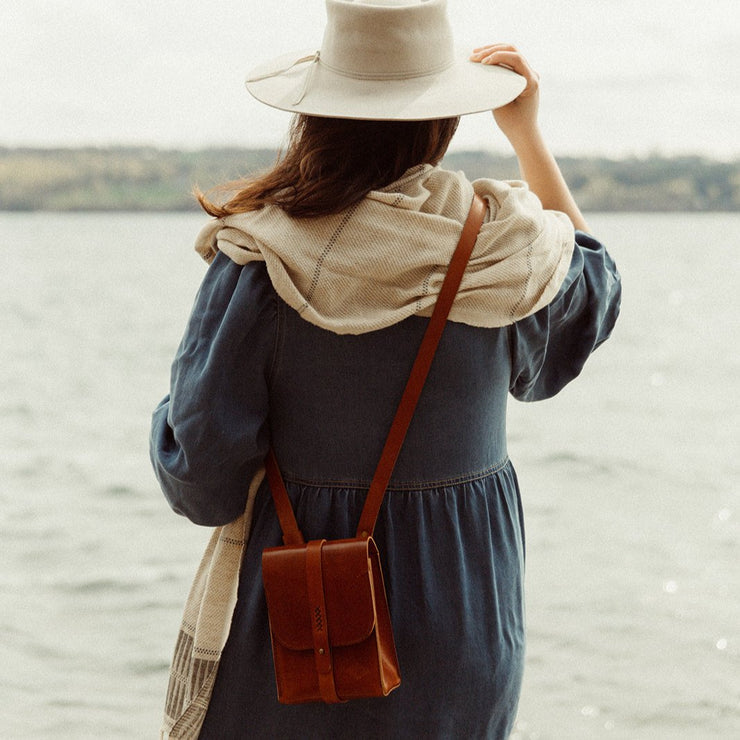 Model wearing cape, hat and leather satchel on the lake