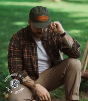 green Canvas 5 panel hat with caramel leather stamped patch with a trout on it