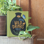 Book titled 'Wild Drinks' by Sharon Flynne on a wooden surface with plants.