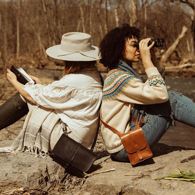 two models wearing the navigator purse and satchel by the creek 